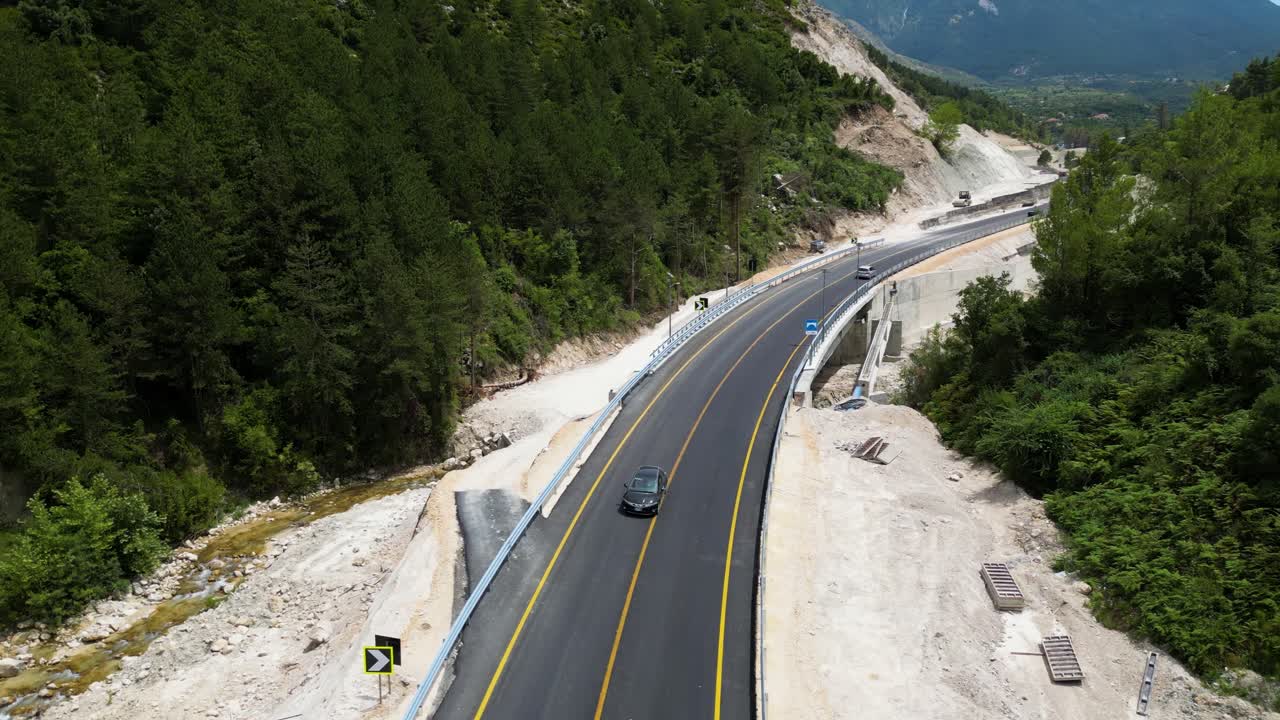 pequeña carretera de montaña con pocos coches que circulan por ella y rodeada de bosque