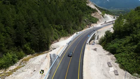 small mountain road with few cars driving on it and surrounded by forest