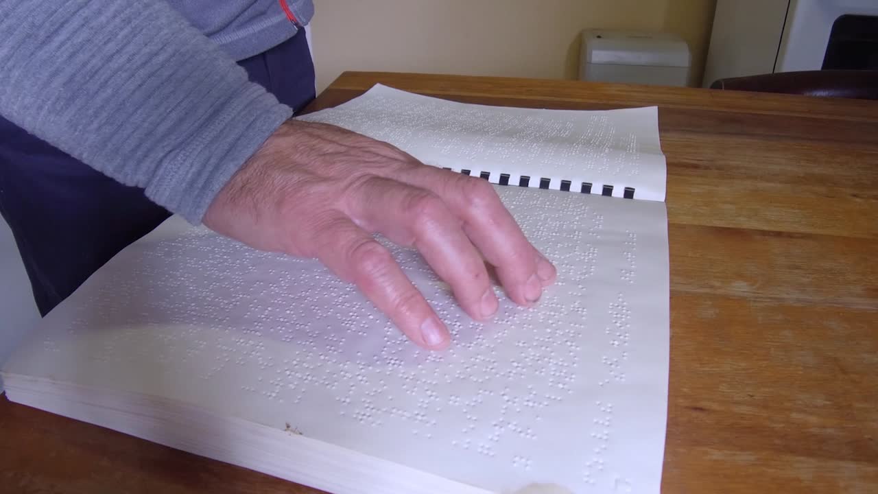 Blind man passes his hand over a book to read braille.