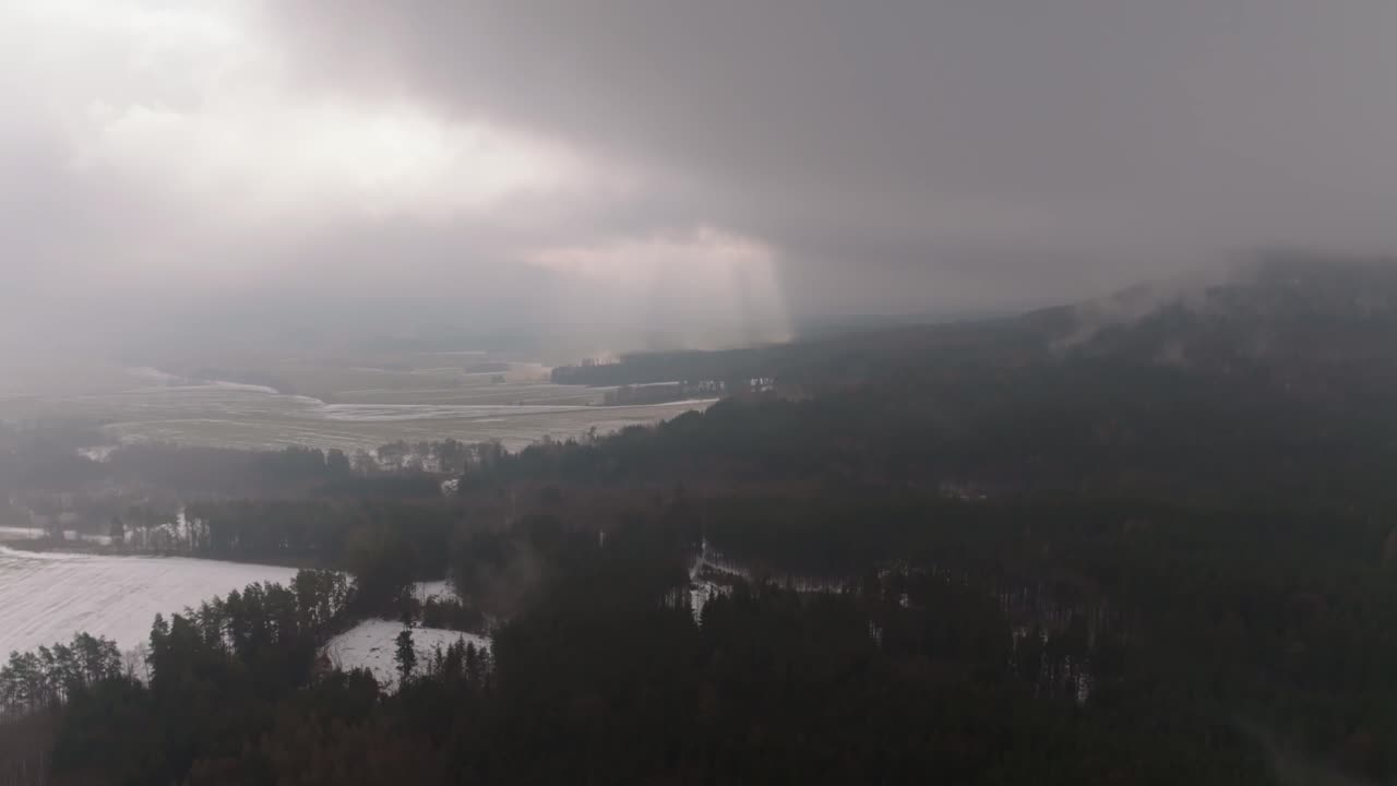 Aerial view of light coming through clouds. Winter panorama of forest and fields landscape in Czech Republic