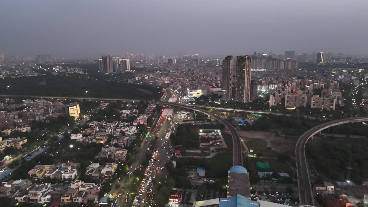 Noida dopo il tramonto, con grattacieli illuminati, cavalcavia trafficati e traffico scorrevole: un ritratto aereo di infrastrutture, crescita ed energia metropolitana incessante