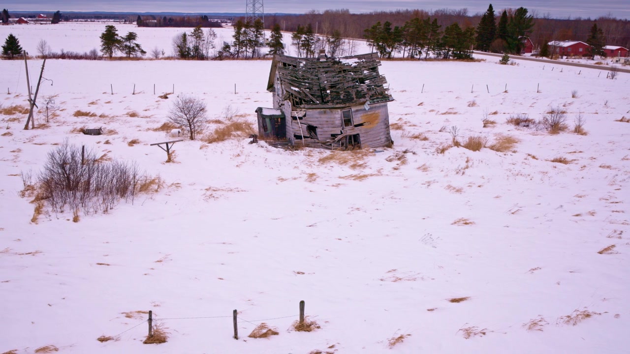 Ripresa da drone che panoramica su un paesaggio invernale con un vecchio fienile fatiscente.