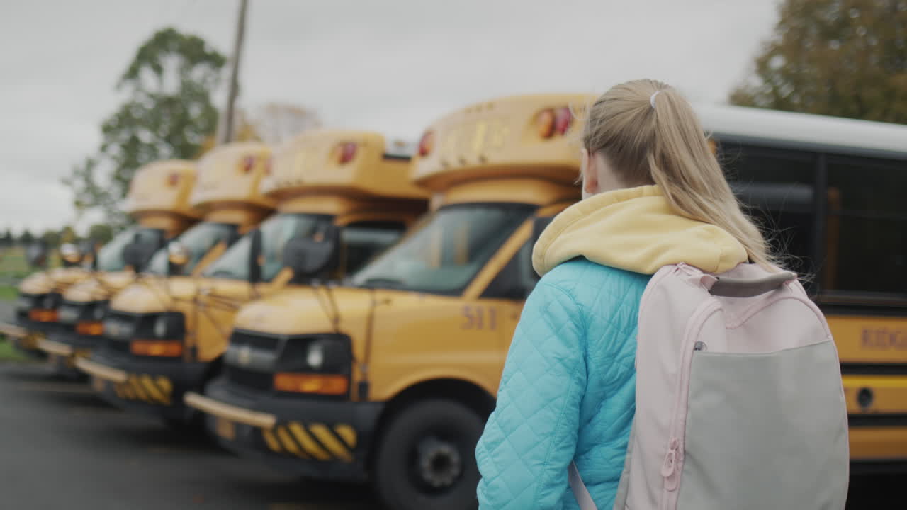 студент идет вдоль ряда желтых школьных автобусов