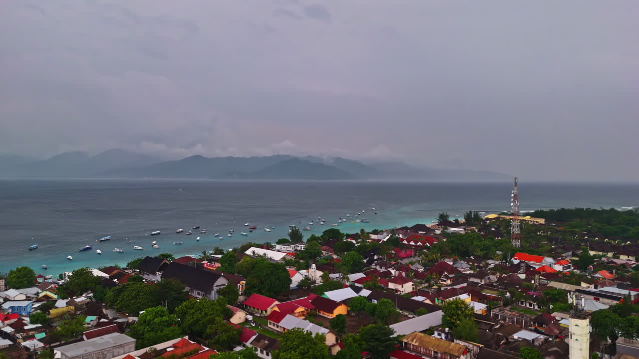 Pemandangan drone di atas kota pesisir Lombok dengan pelabuhan, masjid, perahu, dan pegunungan Bali di cakrawala. Lombok, Indonesia.