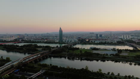 Donauinsel-and-Vienna-city-skyline-at-blue-hour-dusk,-gradient-sky-behind,-aerial-orbit