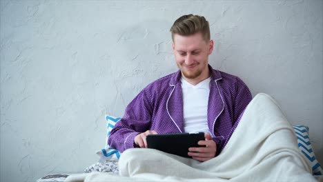 man in pajamas using tablet in bed