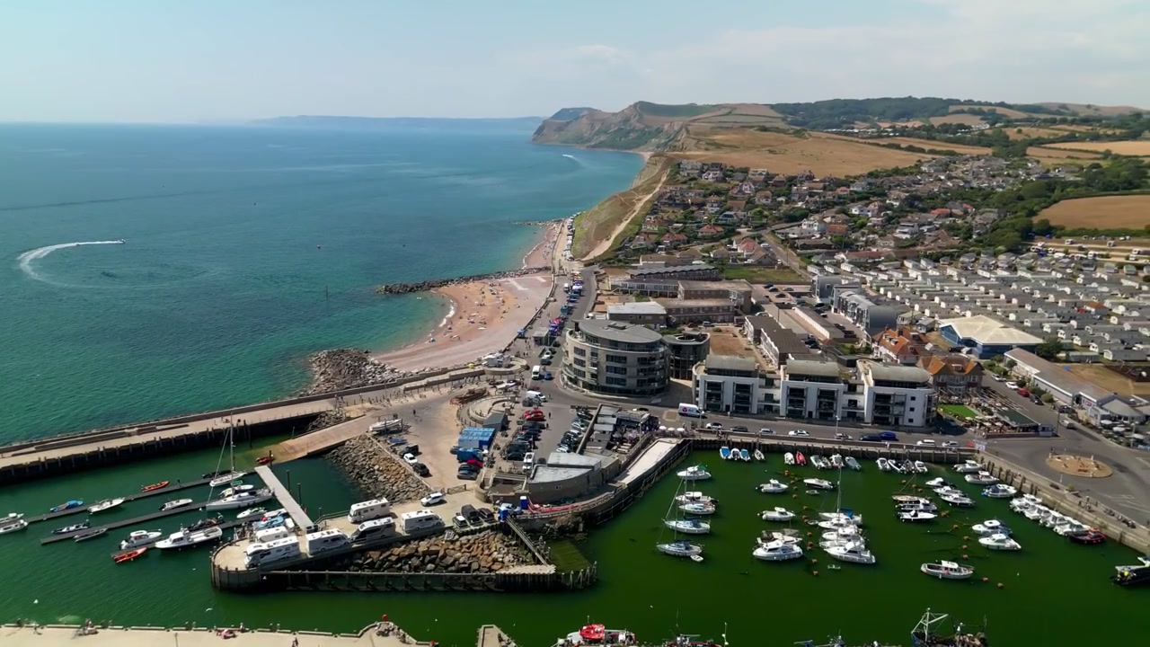 Veduta aerea con drone di West Bay nel Dorset, Inghilterra, che mostra porto, marina, spiaggia, costa, città costiera e Canale della Manica lungo la Costa Giurassica.