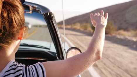 Woman-in-the-front-passenger-seat-of-open-top-car,-back-view