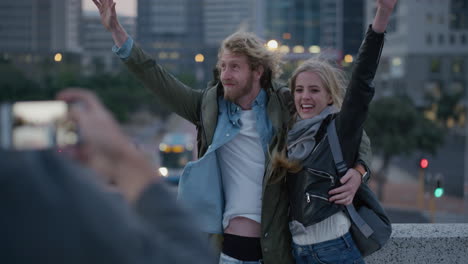 portrait happy young couple posing for photo arms raised celebrating successful travel lifestyle smiling cheerful enjoying vacation together embracing in city at sunset slow motion