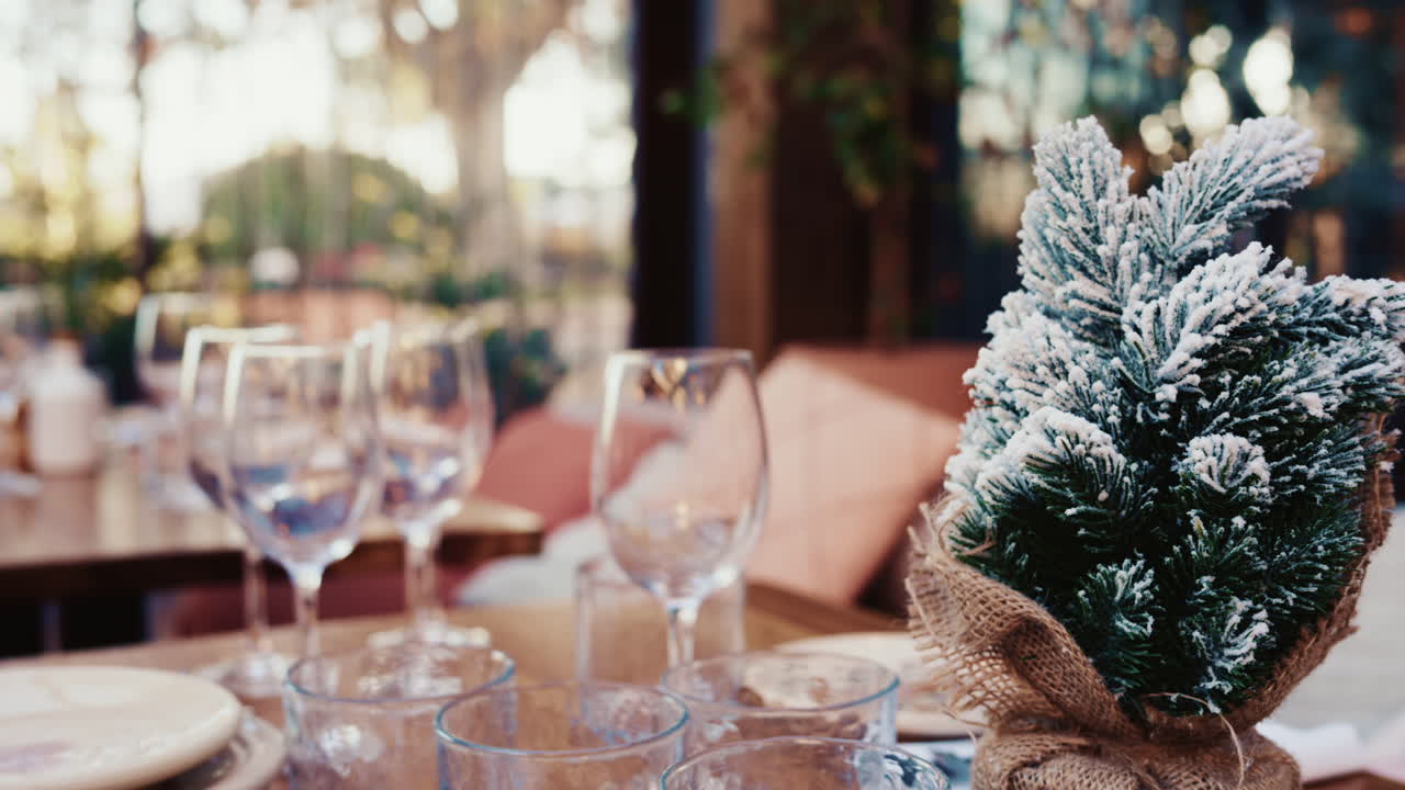 Cozy table setting with glassware and a small snow covered Christmas tree decoration at a resturant