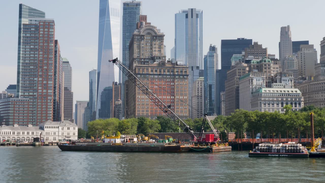 Slow motion landscape of crane barge ship on harbour foreshore wharf in the Battery Park Hudson river New York city skyline CBD towers skyscrapers of Manhattan USA America urban