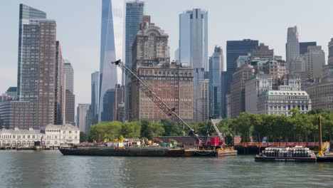 slow motion landscape of crane barge ship on harbour foreshore wharf in the battery park hudson river new york city skyline cbd towers skyscrapers of manhattan usa america urban