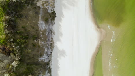 aerial shot looking down over bright white sand beach with green ocean water on baltic sea