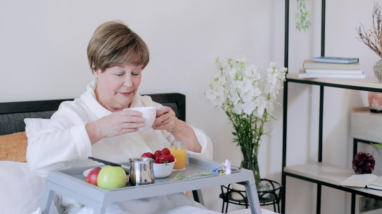 Un'anziana signora versa e beve il caffè a letto durante la colazione