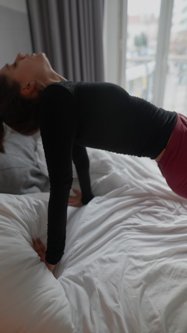 Woman in red leggings and black top stretching on a bed
