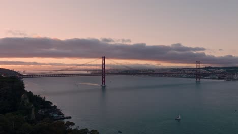 large shot of the bridge of 25 april in lisboa during sunset with the almada at the front.