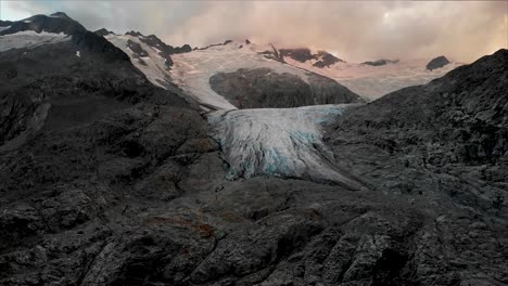 aerial flight over the glacial lake starting with an up close view of the of the gauli glacier in the bernese oberland region of the swiss alps as the sun sets on a cloudy day