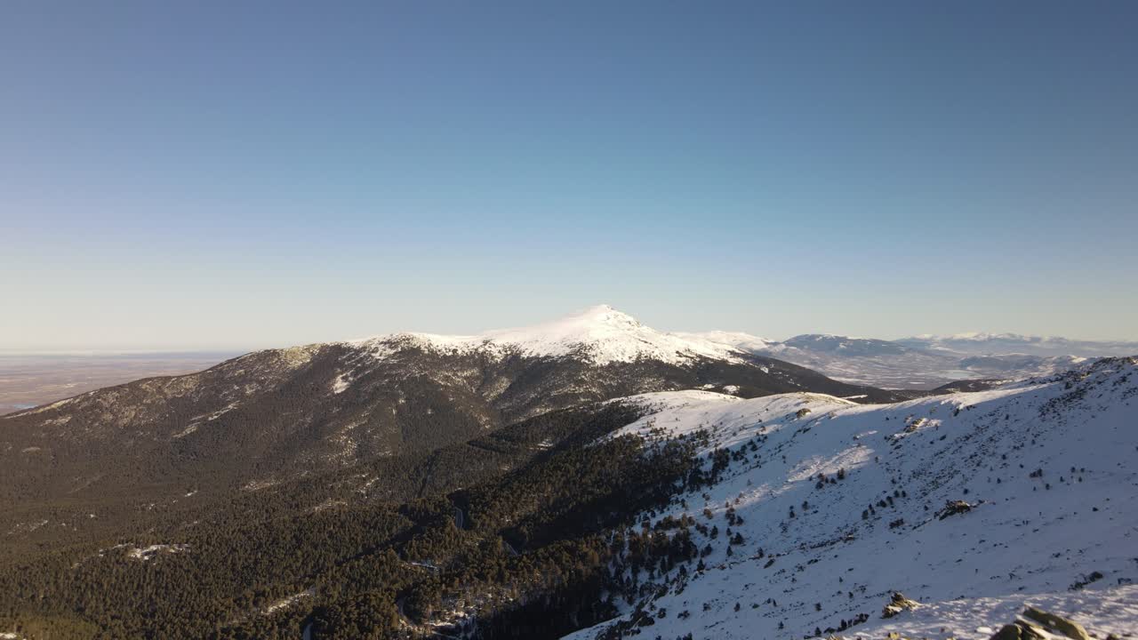 Ripresa aerea con drone in decollo da una strada innevata che rivela una catena montuosa selvaggia e innevata infinita.