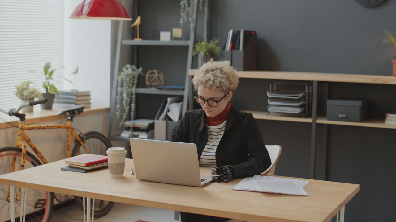 Woman with Prosthetic Arm Working on Laptop in Office