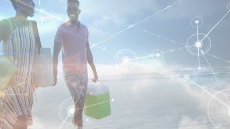 beach couple walking barefoot holding cooler, tote bag and towel, showing network overlay for tech