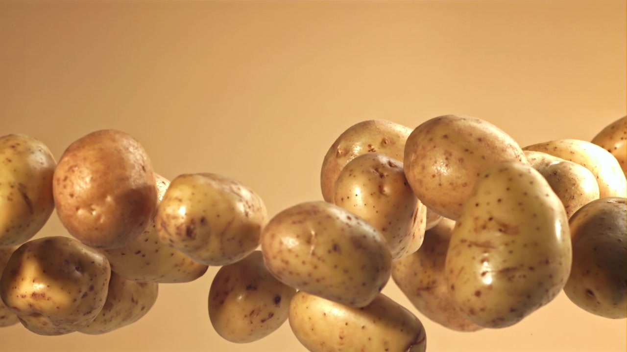 Patate crude che salgono al rallentatore su sfondo neutro