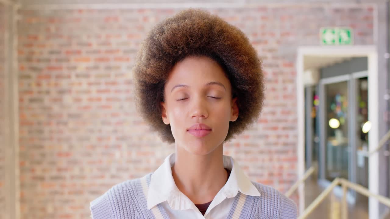 Portrait of biracial creative businesswoman with afro smiling in casual office, slow motion