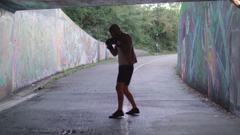 young active man boxing in underpass, silhouetted by light