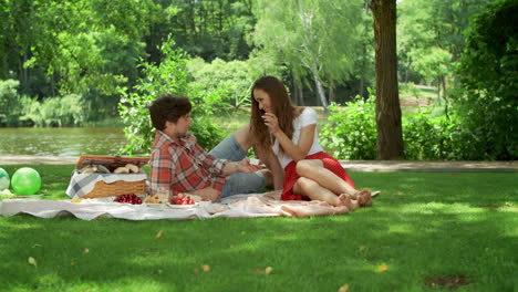 boyfriend and girlfriend eating cherries at picnic. couple relaxing outdoors