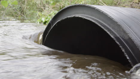 rainwater runoff flows into big black drainage pipe in countryside, telephoto