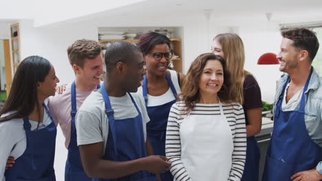 group of smiling men and women wearing aprons taking part in kitchen cookery class