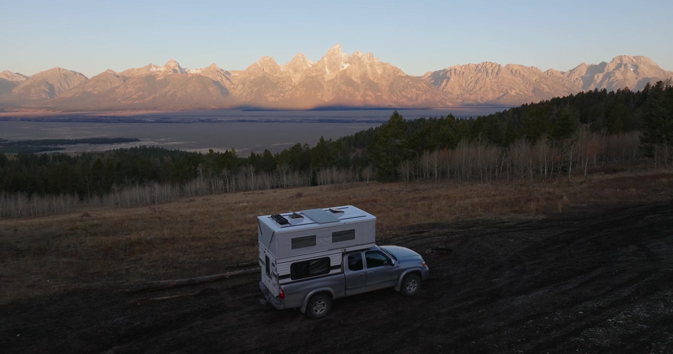 Truck camper parked on dirt road toward Grand Teton mountains at golden hour