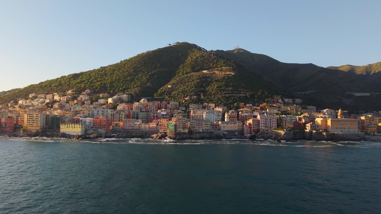 Coastal city with colorful buildings, ocean waves, and hills captured during sunset