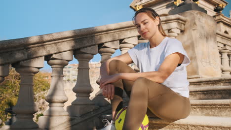 Beautiful-woman-with-ball-in-hands-sitting-on-stairs-in-city-park.