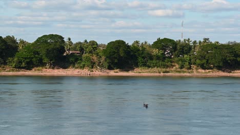 Un-Barco-De-Pesca-Bajando-Por-El-Río-Mientras-El-Pescador-Lanza-Su-Red,-Río-Mekong,-Tailandia-Y-Laos