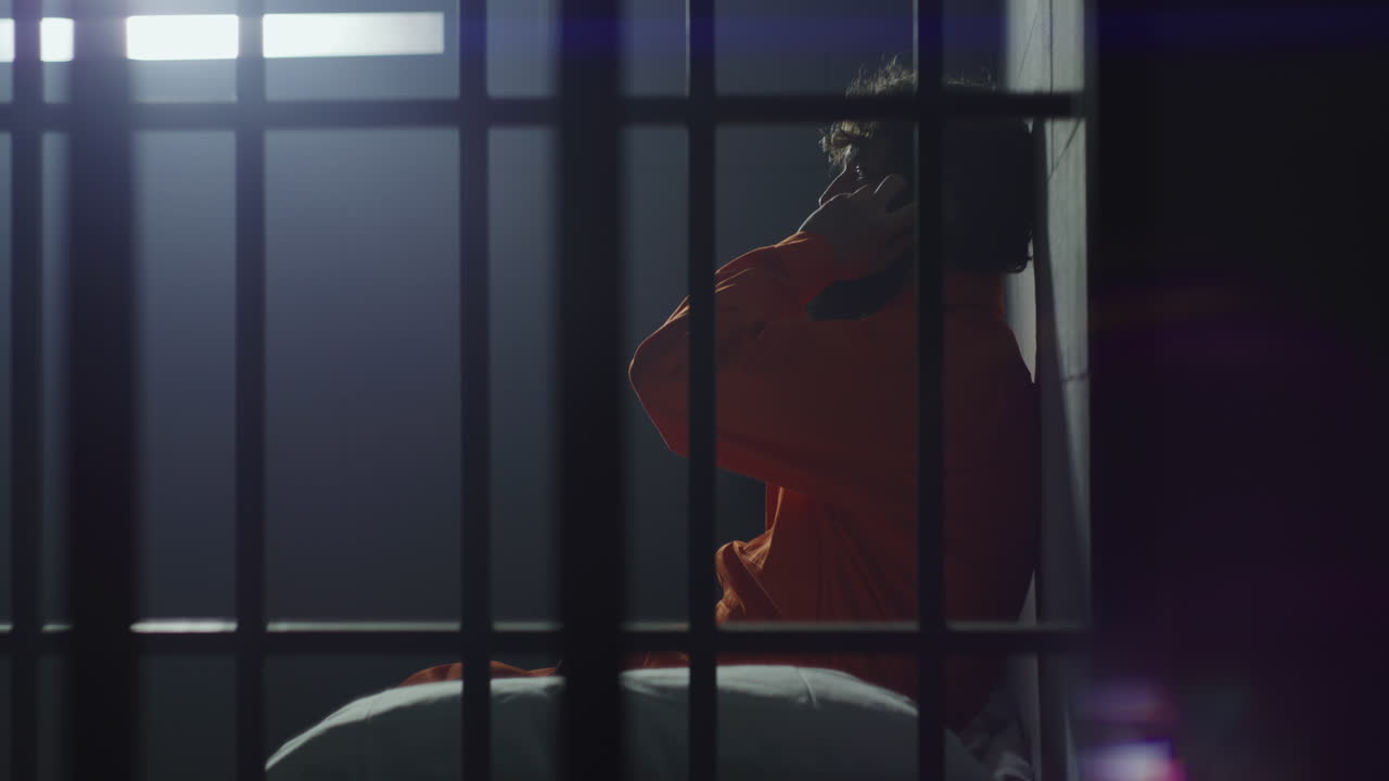 el prisionero se sienta en la cama y habla por teléfono en la celda de la prisión.