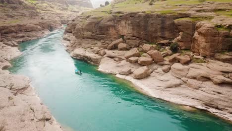 boat-riding-on-a-green-emerald-color-river-water-in-a-clay-rock-cliff-valley-in-nature-cloudy-weather-sky-water-park-adventure-erosion-in-Iran-wonderful-natural-desert-country-outdoor-wild-landscape