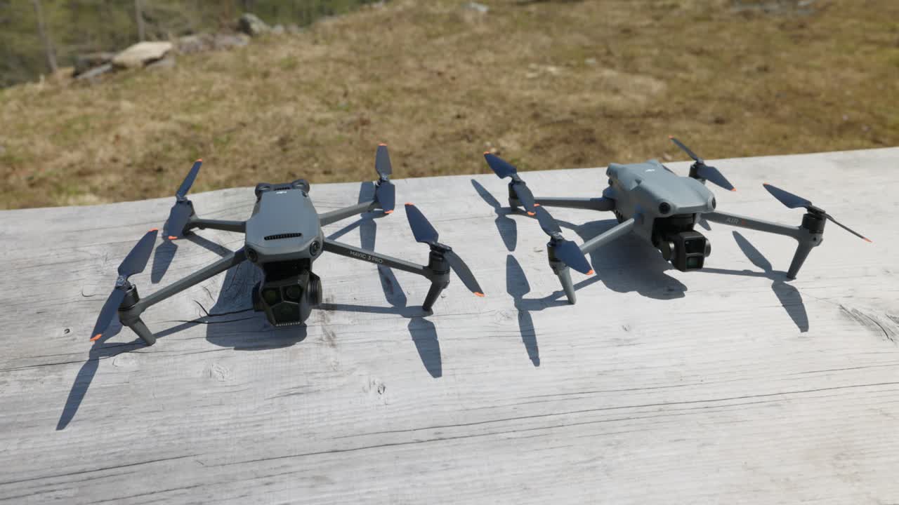 Two consumer camera drones side by side on a wooden table outdoors on sunny day