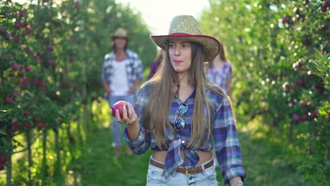 young woman enjoying apples in a sunny orchard with friends