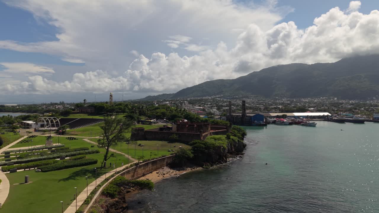 Ripresa cinematografica con drone della storica Fortezza di San Felipe in riva al mare a Puerto Plata, con architettura coloniale, parco costiero e montagne.