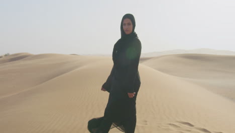 zoom in shot of al muslim woman with hijab looking at camera in a windy desert