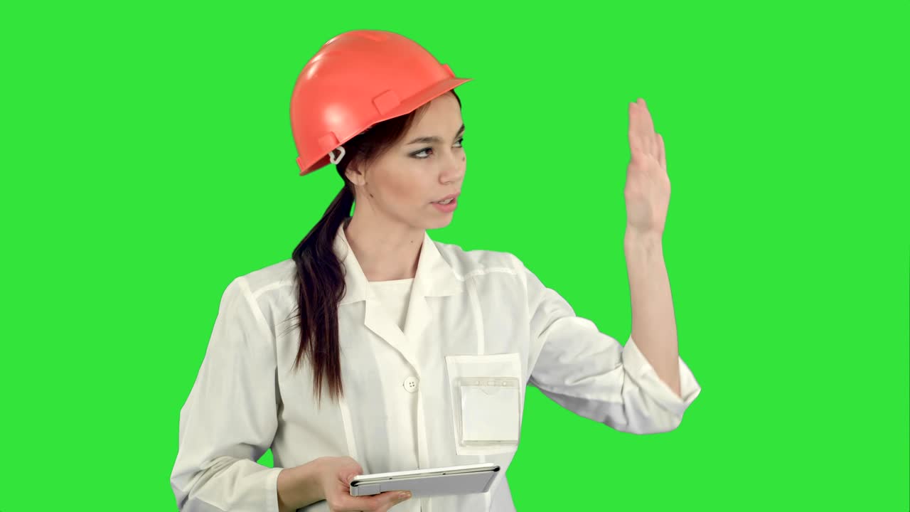디지털 태블릿을 가진 미소 짓는 여성 엔지니어가 녹색 스크린, 크로마 키에서 카메라를 가져갑니다.
