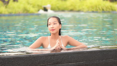 beautiful asian female on pool edge enjoying in nice weather and water on exotic tropical vacation, slow motion