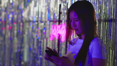 woman checking messages on mobile phone in nightclub or funfair