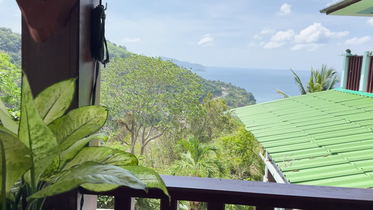 Lush greenery and ocean views from a clifftop restaurant in Phuket, Thailand. Bright daylight enhances the vibrant landscape