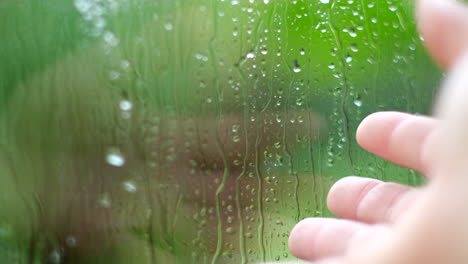 hand gesture appreciates rain falling outdoors with drops running down window