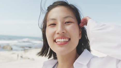 Retrato-De-Una-Mujer-Birracial-Feliz-Sonriendo-En-La-Playa,-En-Cámara-Lenta