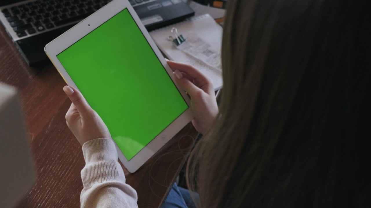 vista desde detrás del hombro de la tableta con pantalla verde, la niña sostiene el gadget en las manos, mira la pantalla, utiliza medios de comunicación, recurso de medios, hombro, lectura, búsqueda, freelance, estudio