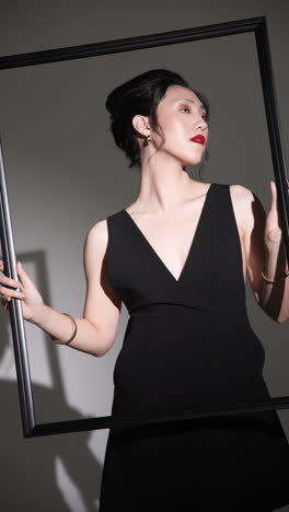 vertical video: elegant woman in black dress posing with frame, showcasing modern fashion style