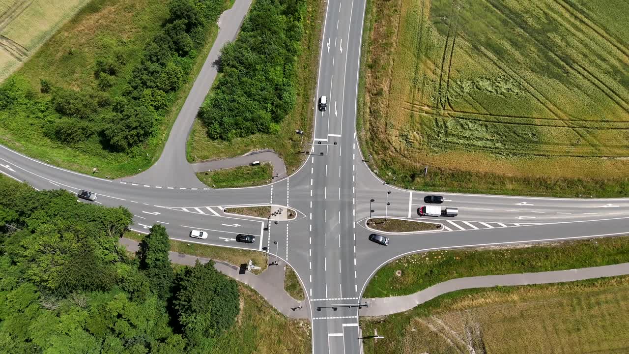 Junction with cars in suburb of American town. Green grass fields in rural area. Aerial top down rising shot. Sunny day in summer season. Stopping vehicle, USA.