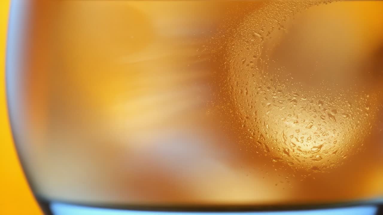 Slowly panning camera revealing chilled glass covered in droplets in studio showing cold beverage